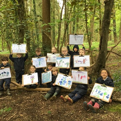 A group of reception children holding up their paintings of  bluebells in our local woods