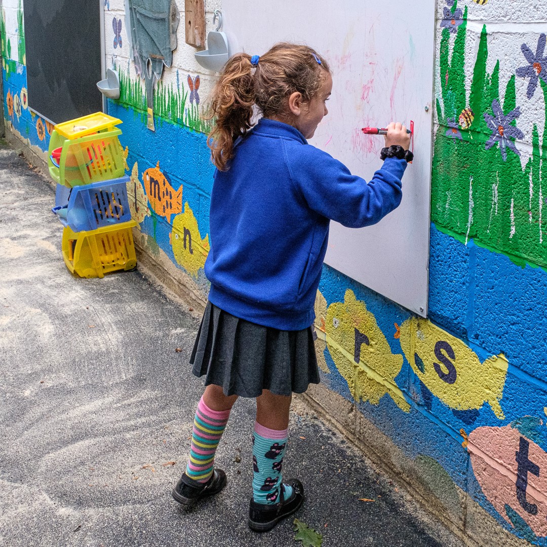 Early years pupil writing on the outdoor whiteboard